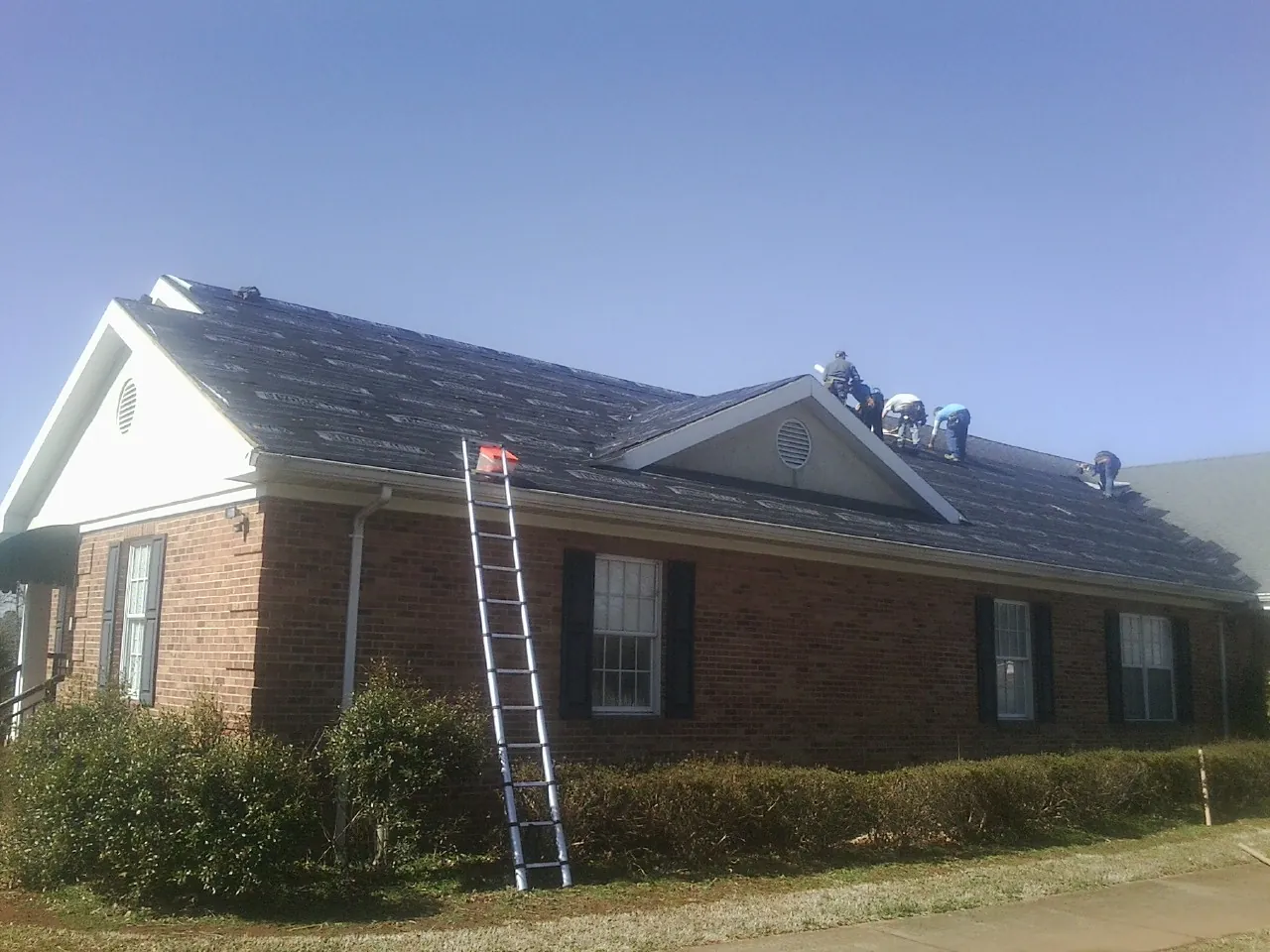 Crew tearing shingles off a brick ranch roof with a ladder set — Metal Roof Repair work by our crew in Peoria Heights