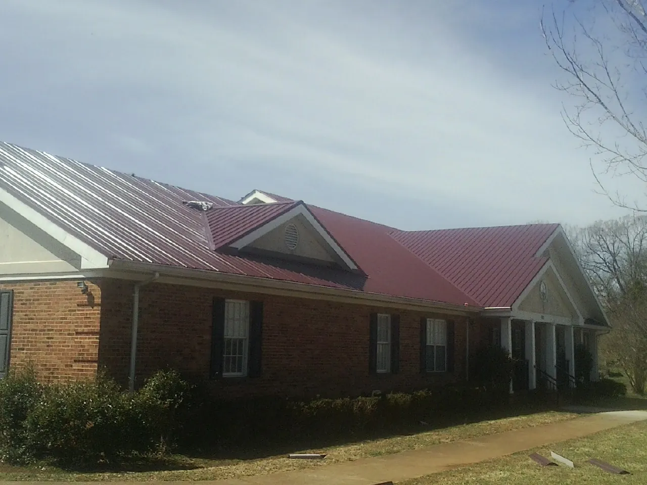 Red metal roof with gabled entries on a long brick building, from a Hail Damage Roof Repair job in Peoria Heights