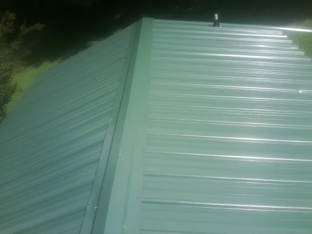 New green metal panels meeting at the ridge of a roof — Flat Roof Repair work by our crew in Peoria Heights