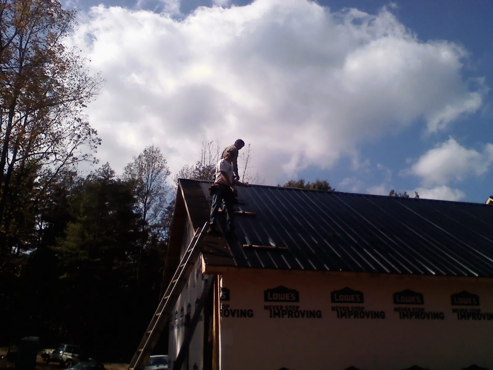 Roofer fastening dark metal panels high against a cloudy sky, from a Roof Inspection job in Peoria Heights