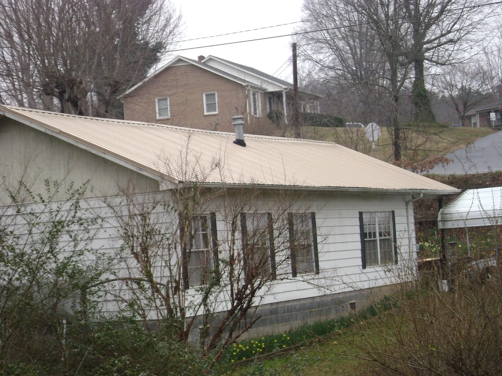 Tan metal roof on a white sided house set into a hillside — Commercial Roofing by Roofing Brothers in Peoria Heights