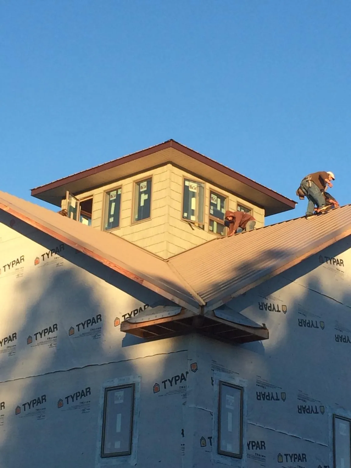 Roofers working around a rooftop cupola on a new metal roof at sunset — Roof Waterproofing in Peoria Heights by Roofing Brothers